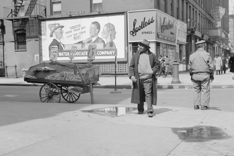 A man in a hat crosses a street and walks by a wagon and "Spotless Stores."