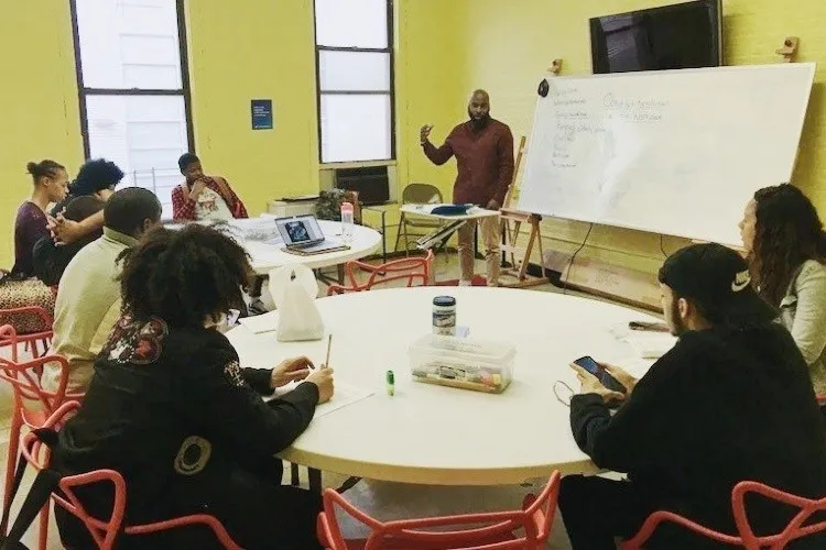 Instructor with students at round tables watching. 
