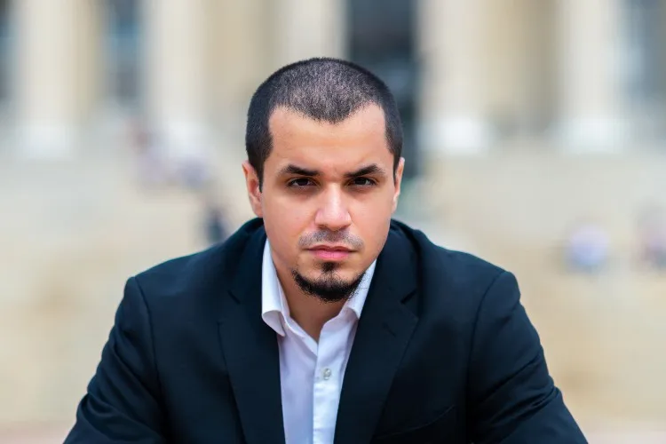 A young man with short hair in a suit jacket.