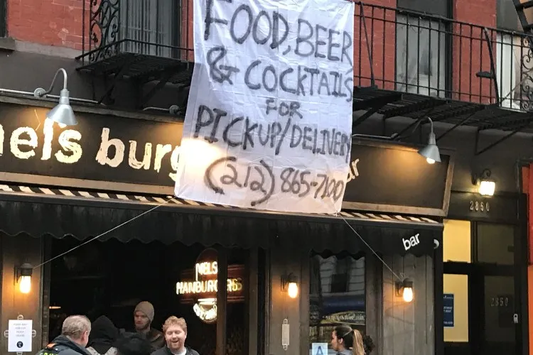 Image of Mel's Burger storefront with hand written banner overhanging fire escape giving pickup delivery instructions. 