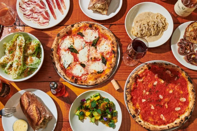 Photo of table with multiple dishes on it, featuring two pizzas.