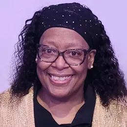 A woman smiles and poses for a photo in front of a purple background. 