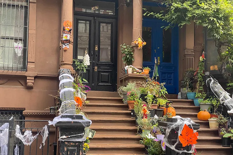 A photo of a stoop in Harlem with cobwebs, pumpkins, and flowers. 