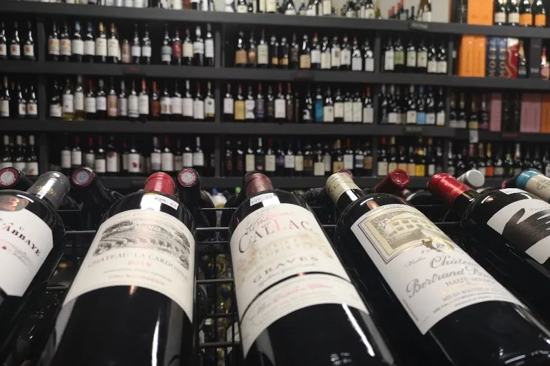 Wine bottles lying down close to the camera, with wall shelves full of other wine bottles in the background.