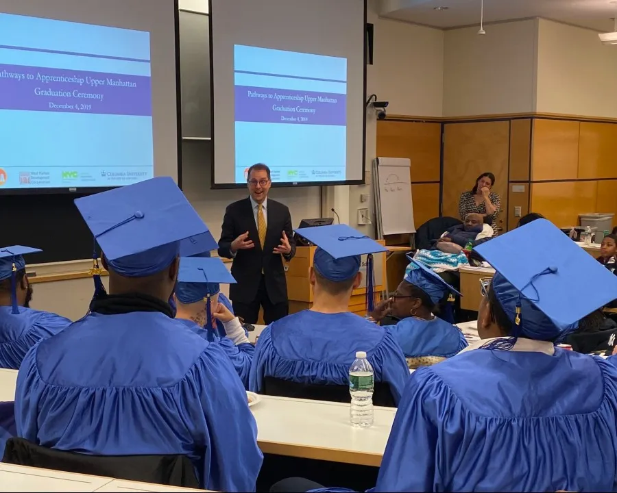 Councilmember Mark Levine speaks to a room of P2A graduates in caps and gowns.