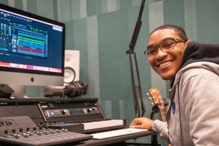 A boy smiles at the camera. He's using a computer with a program open on the screen.
